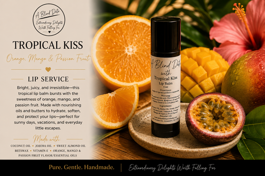 A bottle of Tropical Kiss Lip Balm by A Blind Date is displayed on a wooden tray, surrounded by fresh tropical fruits including sliced oranges, mango, passion fruit, and a pink hibiscus flower. The left side of the image features a text panel detailing the product's ingredients and benefits.